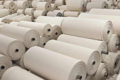 Warehouse racking stacked with rolls of finished white knitted fabric ready for export.
